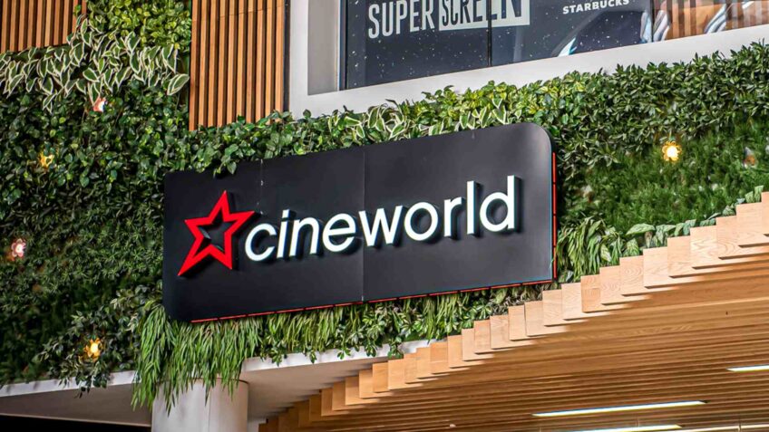 Black Cineworld sign hanging on wall with wooden cladding and green leafy decoration.